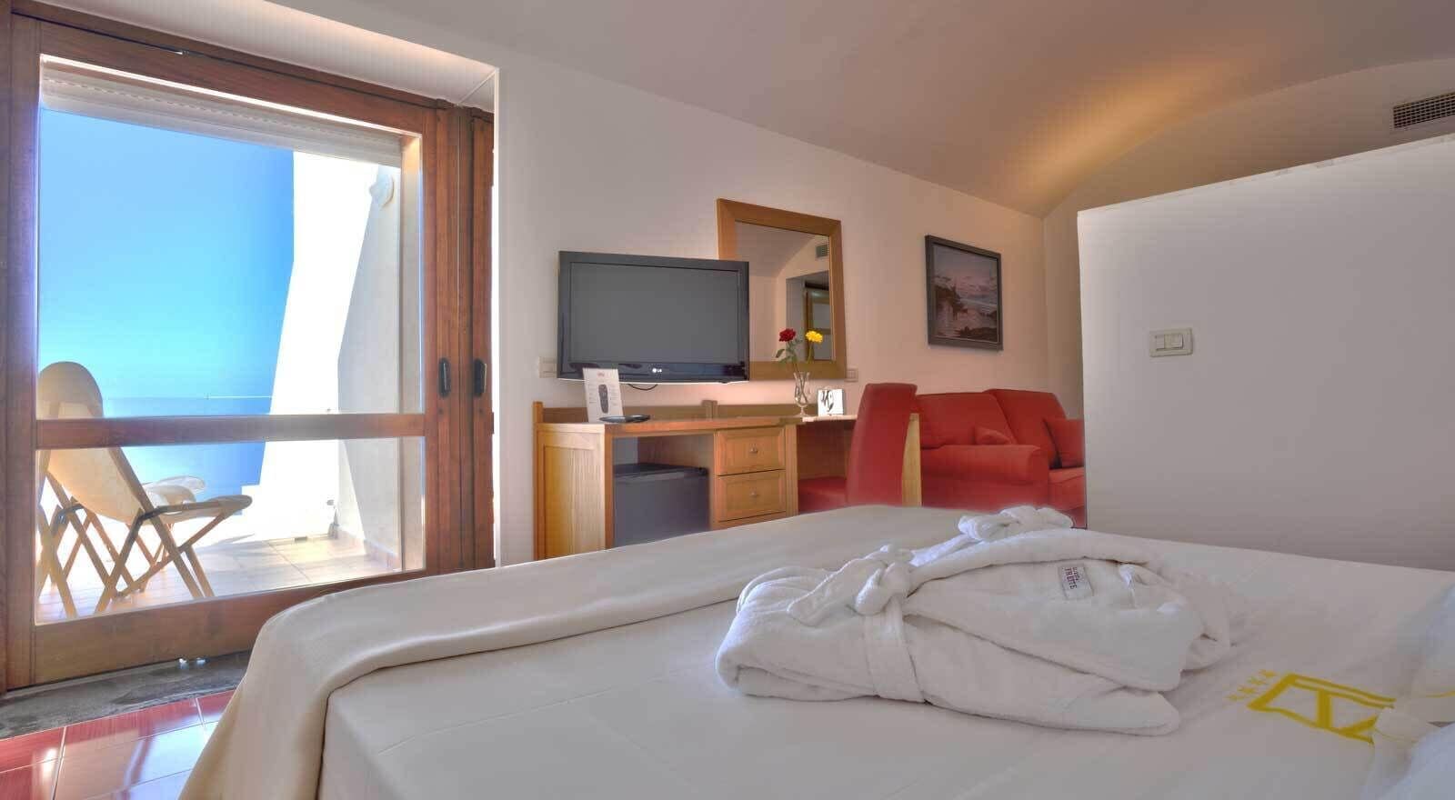 Une chambre d’hôtel avec un lit, un bureau avec une télévision, une chaise et un fauteuil rouge.