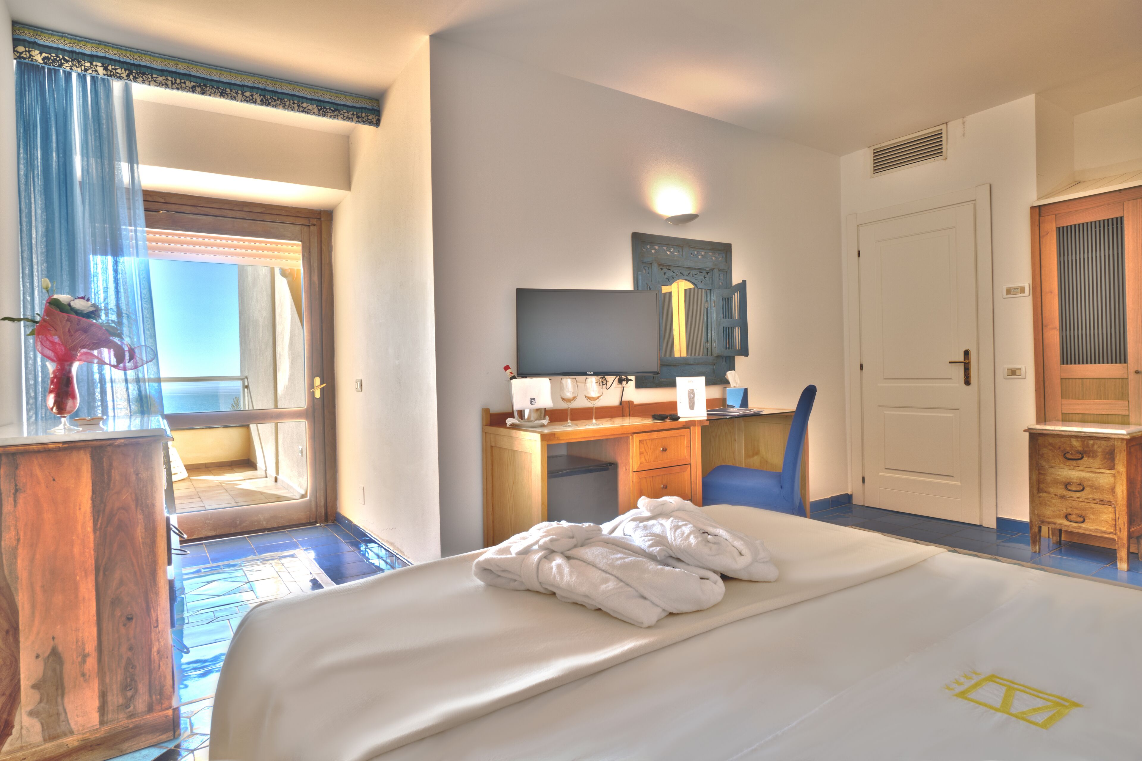 Una camera d'albergo con un letto, una scrivania, una sedia, un armadio e una porta che dà su un balcone.