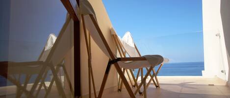 Un balcón con vista al mar, una silla plegable y una pared blanca.