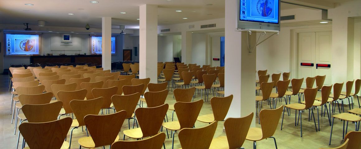 Une salle de conférence avec des rangées de chaises, un écran de projection et un téléviseur.