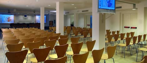 Une salle de conférence avec des rangées de chaises, un écran de projection et un téléviseur.