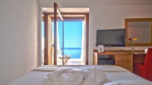 A hotel room with a bed, a desk with a TV, a chair, and a view of the sea. - Grand Hotel San Pietro (Centola)