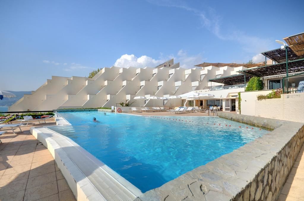 Une piscine au design architectural moderne, entourée de chaises longues et offrant une vue dégagée sur la mer.