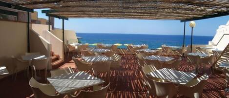 An outdoor seating area with tables and chairs, overlooking the sea.