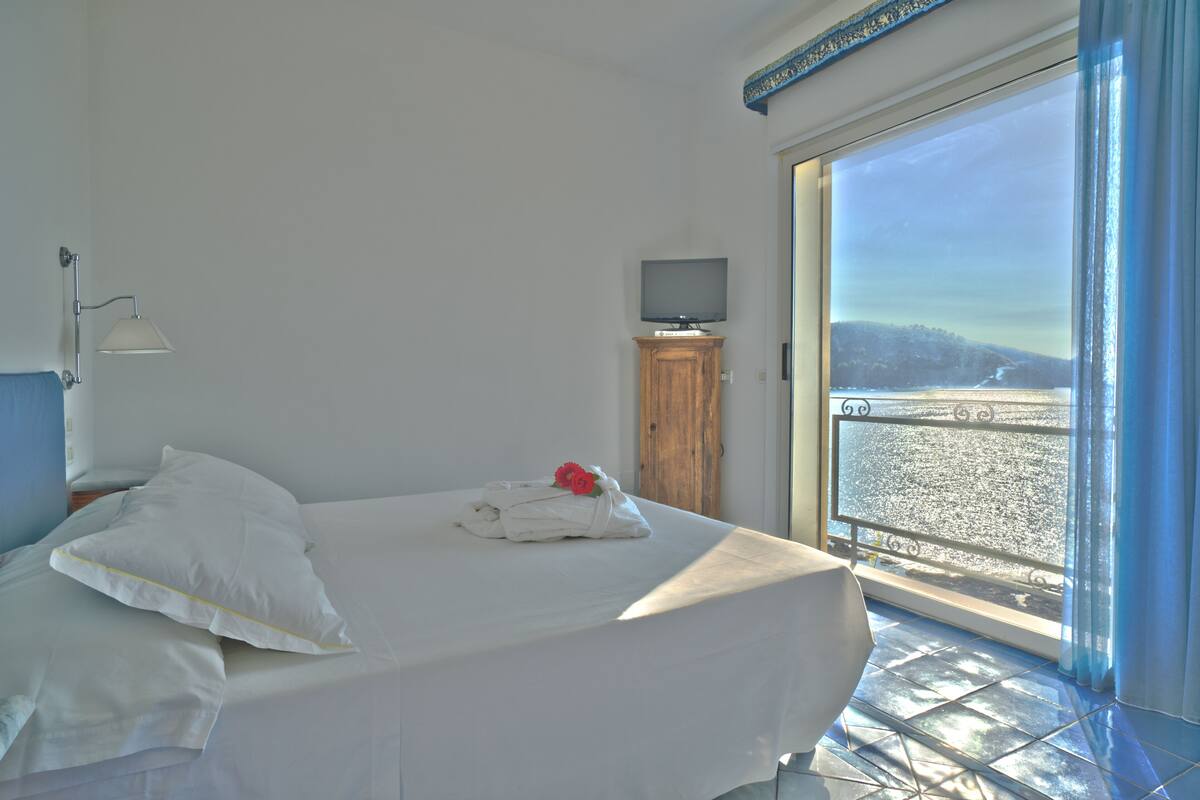 A hotel room with a bed, a TV on a wooden cabinet, and a balcony with a view.
