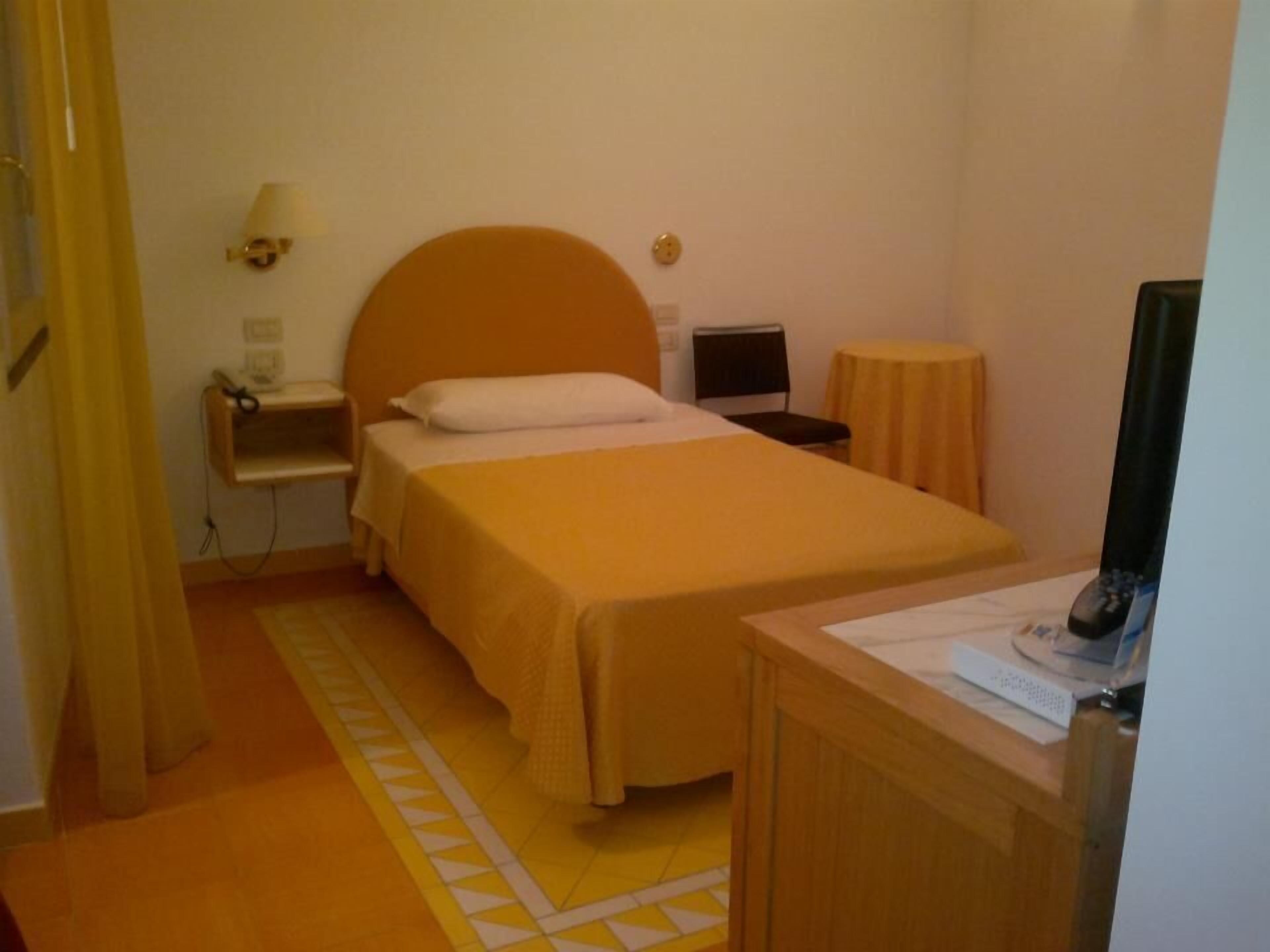 A hotel room with a bed, a desk, a chair, a lamp, and a TV.