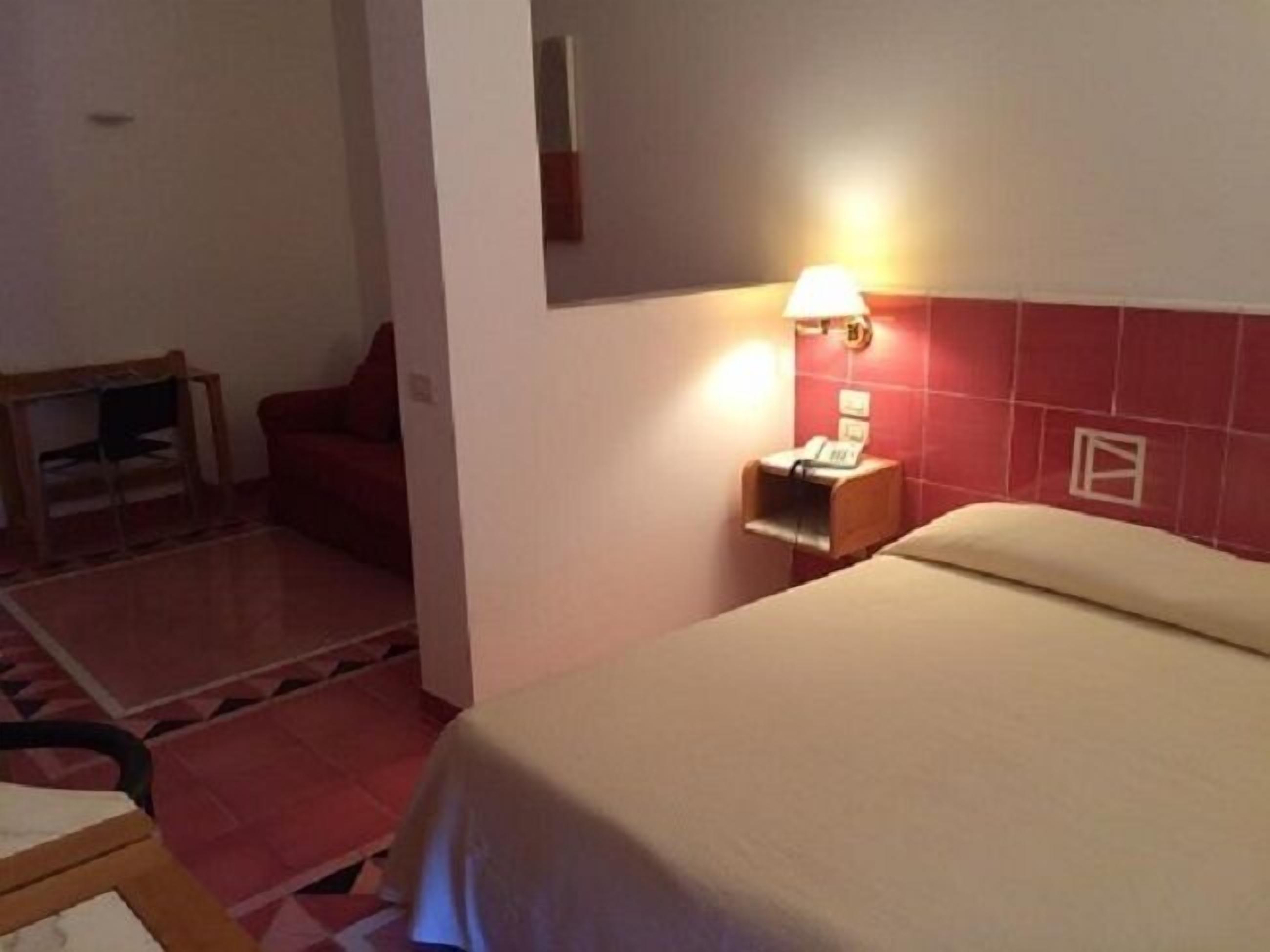 A hotel room with a bed, a nightstand with a lamp, a chair, and a small table.