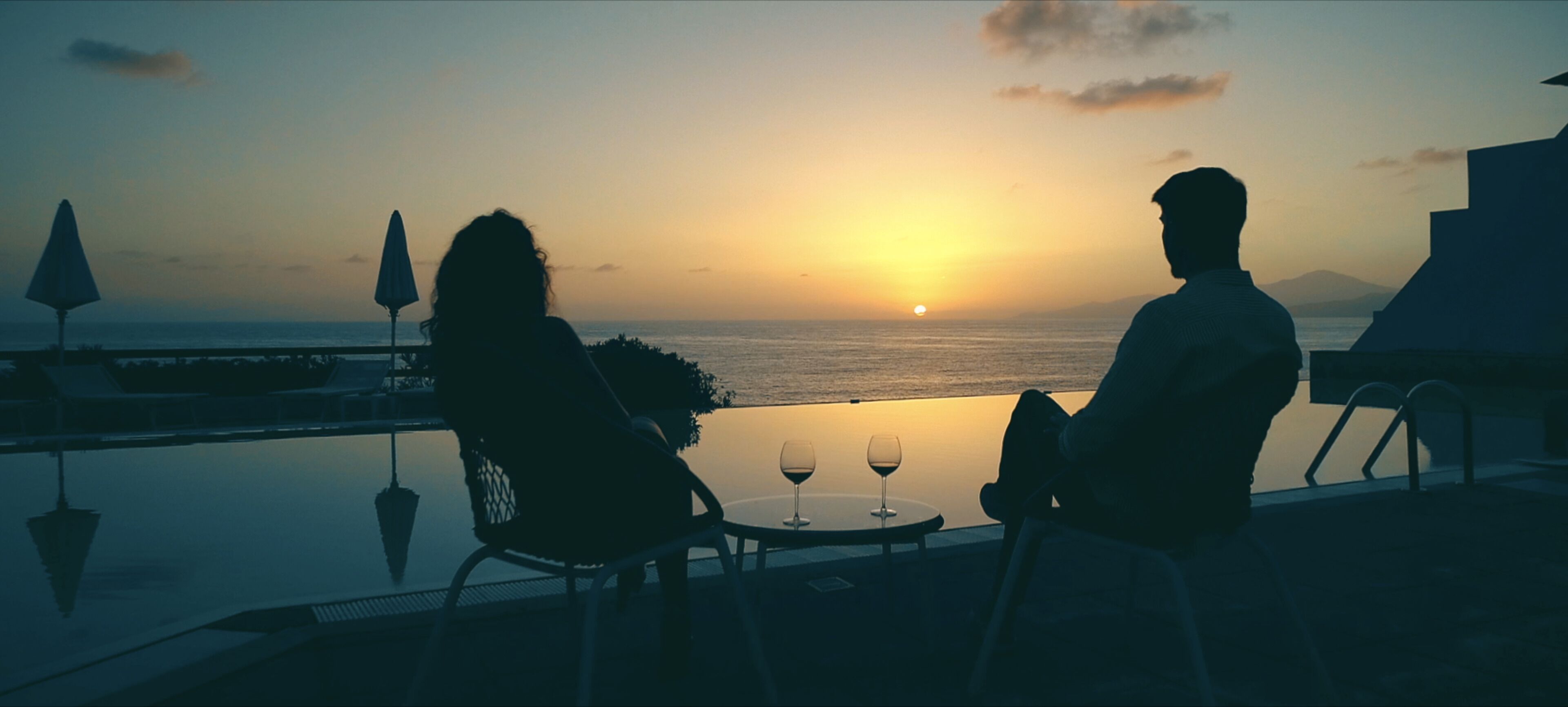 A couple sitting at a table with a view of the sunset over the water.