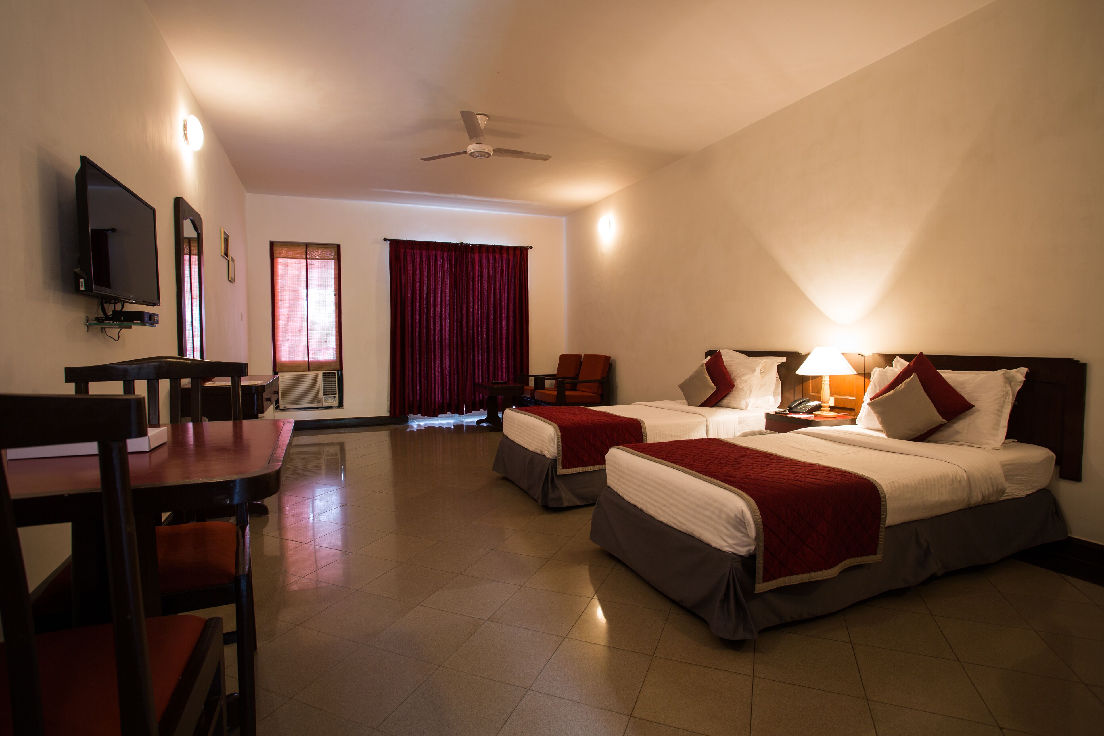 Habitación de hotel con dos camas, un escritorio, una silla, un televisor y un ventilador de techo.