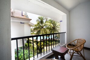 A balcony with a view of a pool and palm trees, a wicker chair, and a small table. - Resort Lagoa Azul (Arpora)