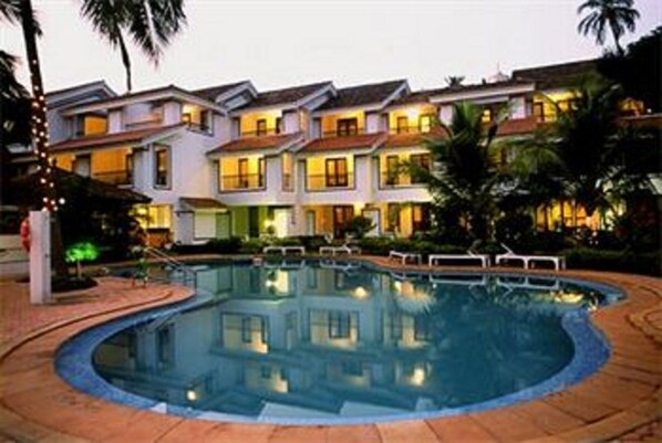 A hotel with a swimming pool, multiple balconies, and palm trees.