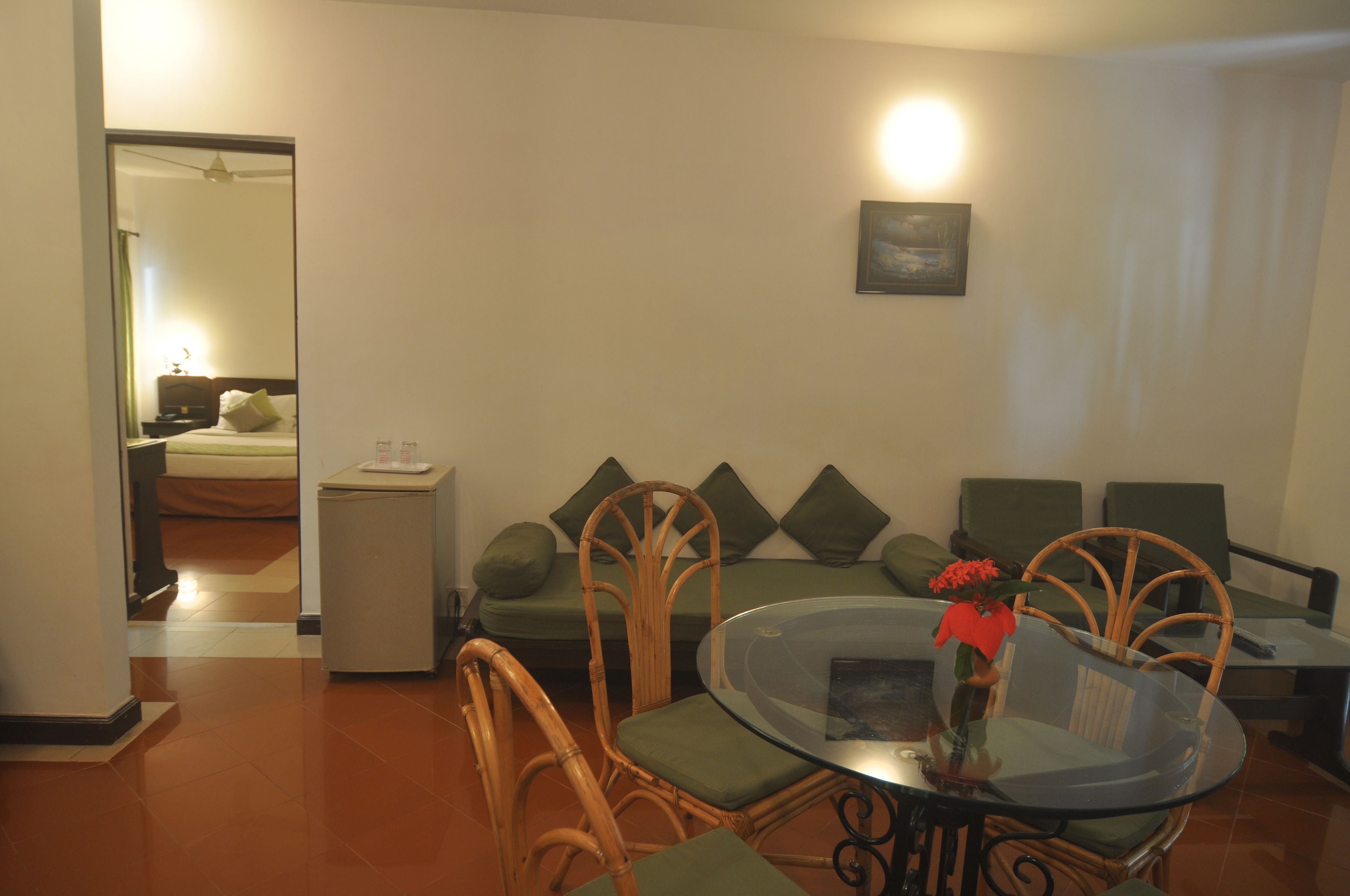 Una sala de estar con una mesa de vidrio, sillas de mimbre, un sofá verde y una pequeña mesa blanca.