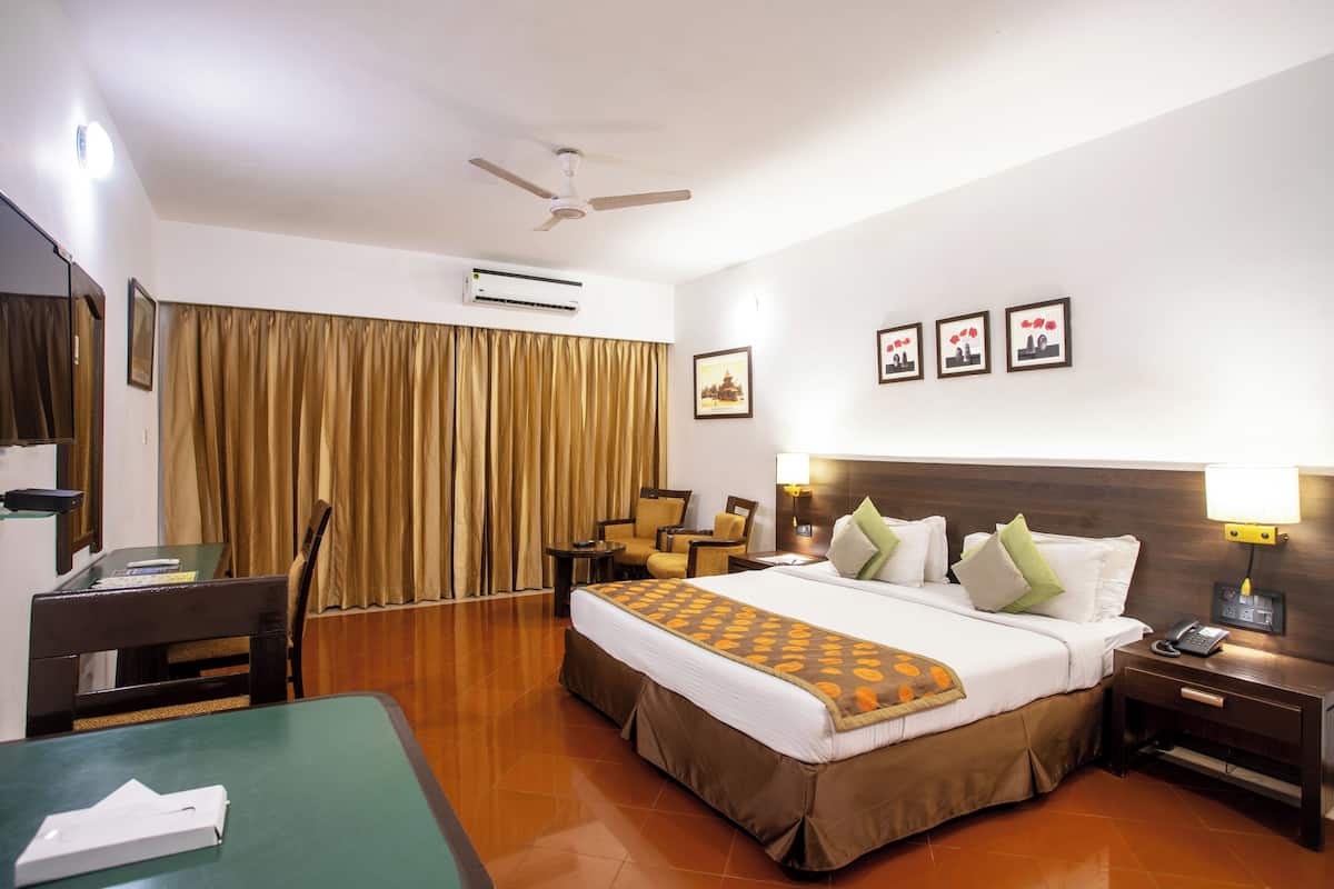 Quarto de hotel com cama, escrivaninha, cadeira, mesa, ventoinha no teto e ar condicionado na parede.
