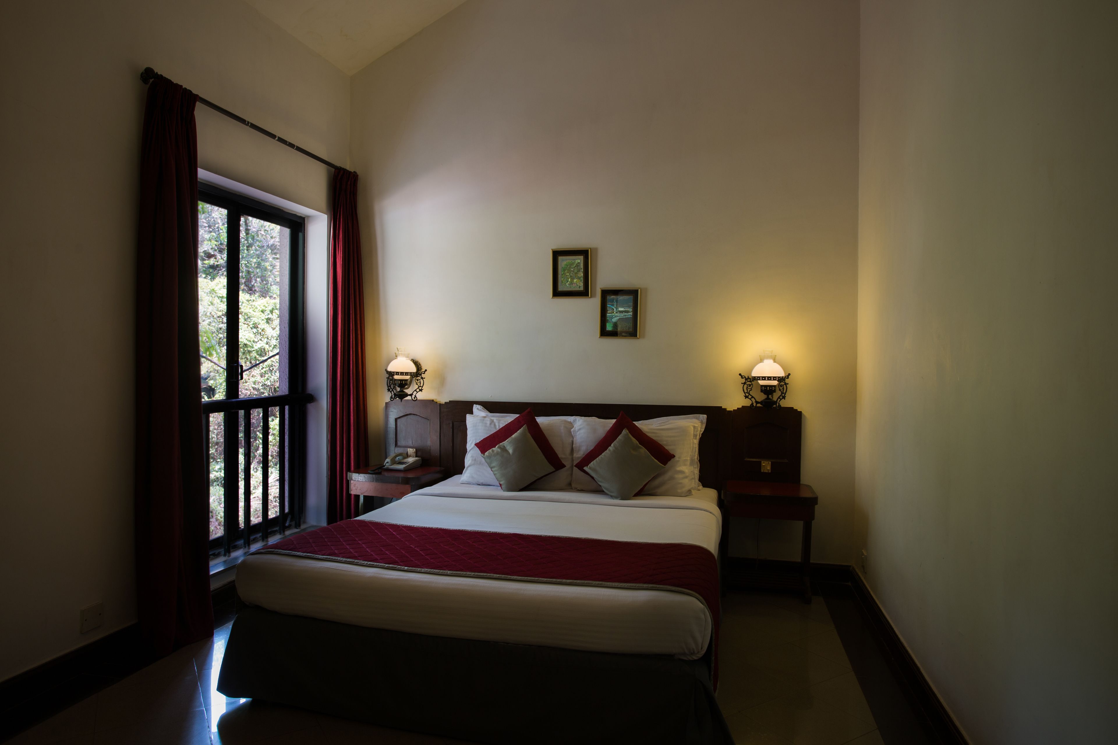 A hotel room with a large bed, two bedside tables with lamps, a window with curtains, and two framed pictures on the wall.