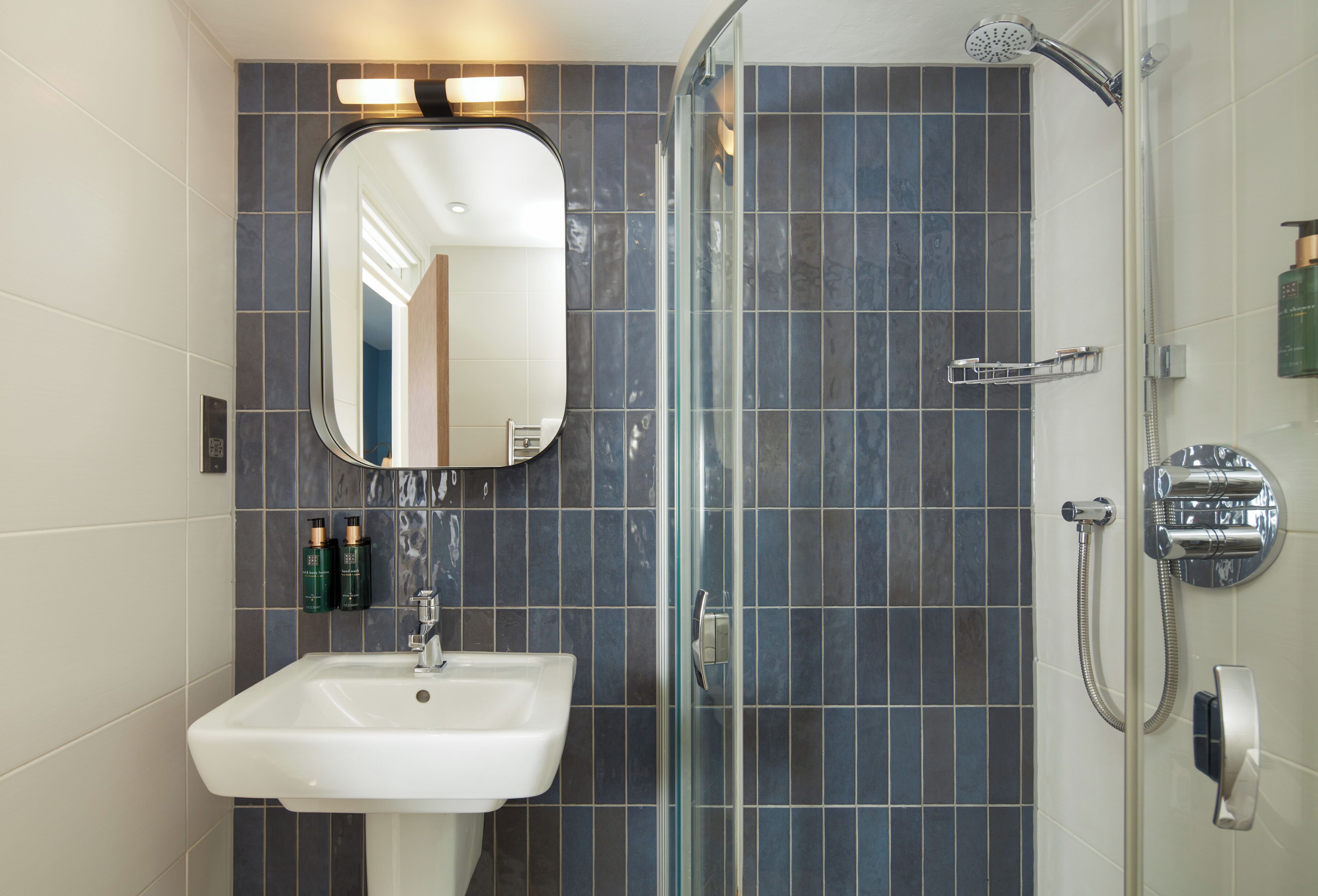 Un baño con cabina de ducha de vidrio, un lavamanos blanco y un espejo sobre él.