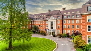 A large brick building with a central entrance, surrounded by well-maintained lawns and trees. - The Lensbury Resort (Teddington)