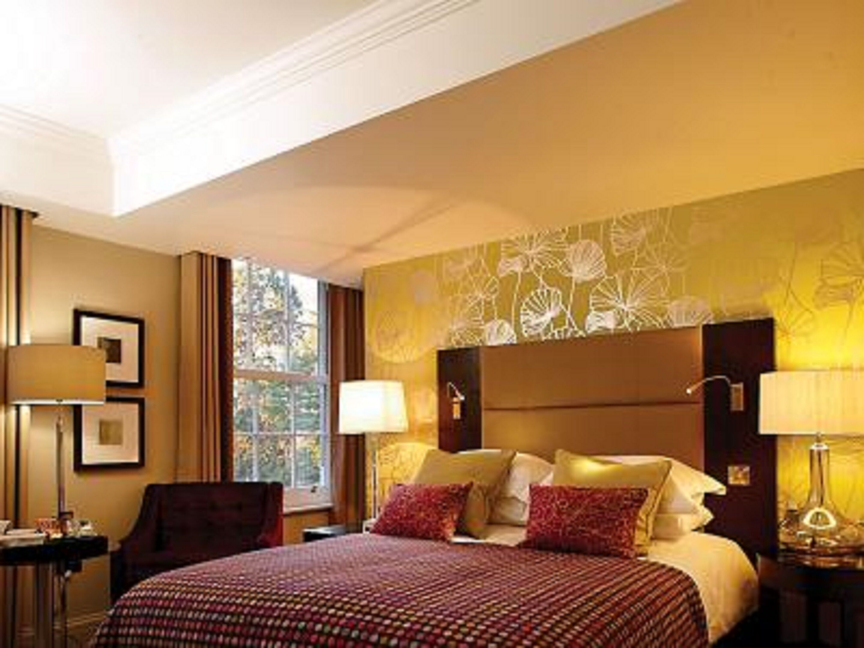 Habitación de hotel con una cama grande, dos lámparas de noche, una silla, una mesita y una ventana con cortinas.