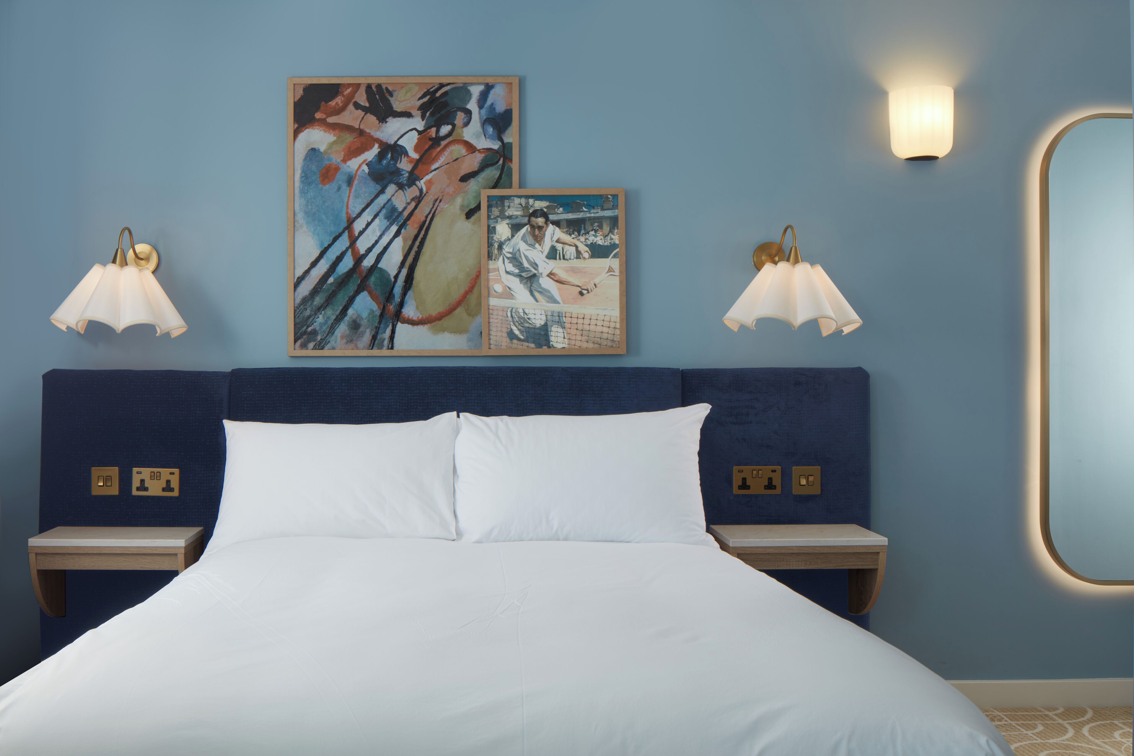 A hotel room with a bed, two nightstands, wall-mounted lamps, and two framed artworks.