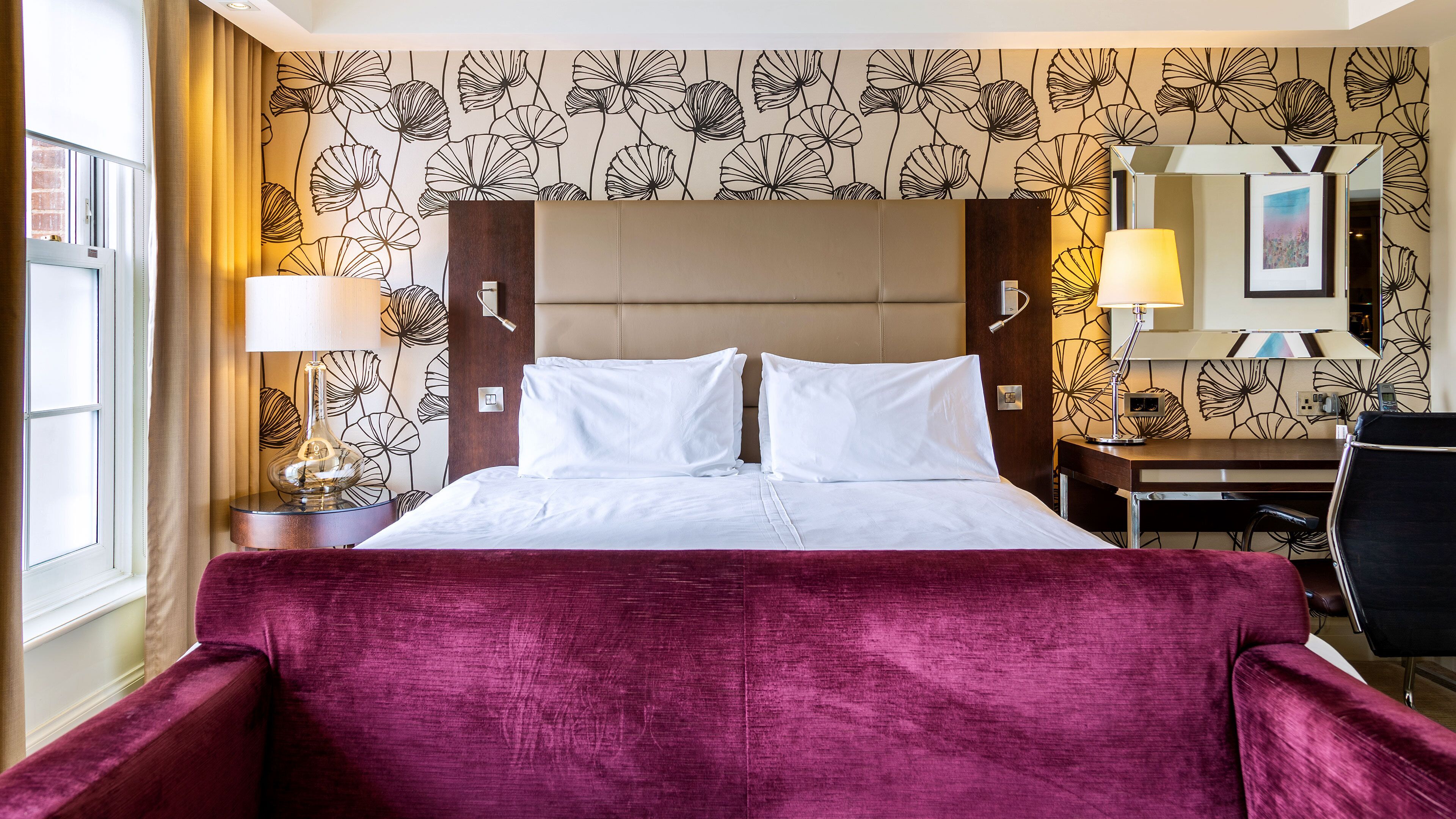 A hotel room with a large bed, a desk, a chair, and a window with curtains.
