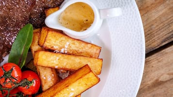 A plate with steak, French fries, a small bowl of sauce, and cherry tomatoes.