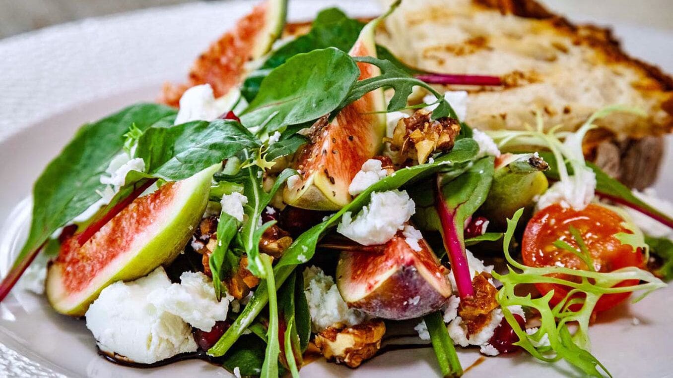 A plate with a salad, figs, and a piece of bread.