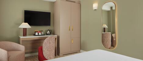 A hotel room with a bed, a desk with a flat-screen TV, a wardrobe, a chair, and a mirror.