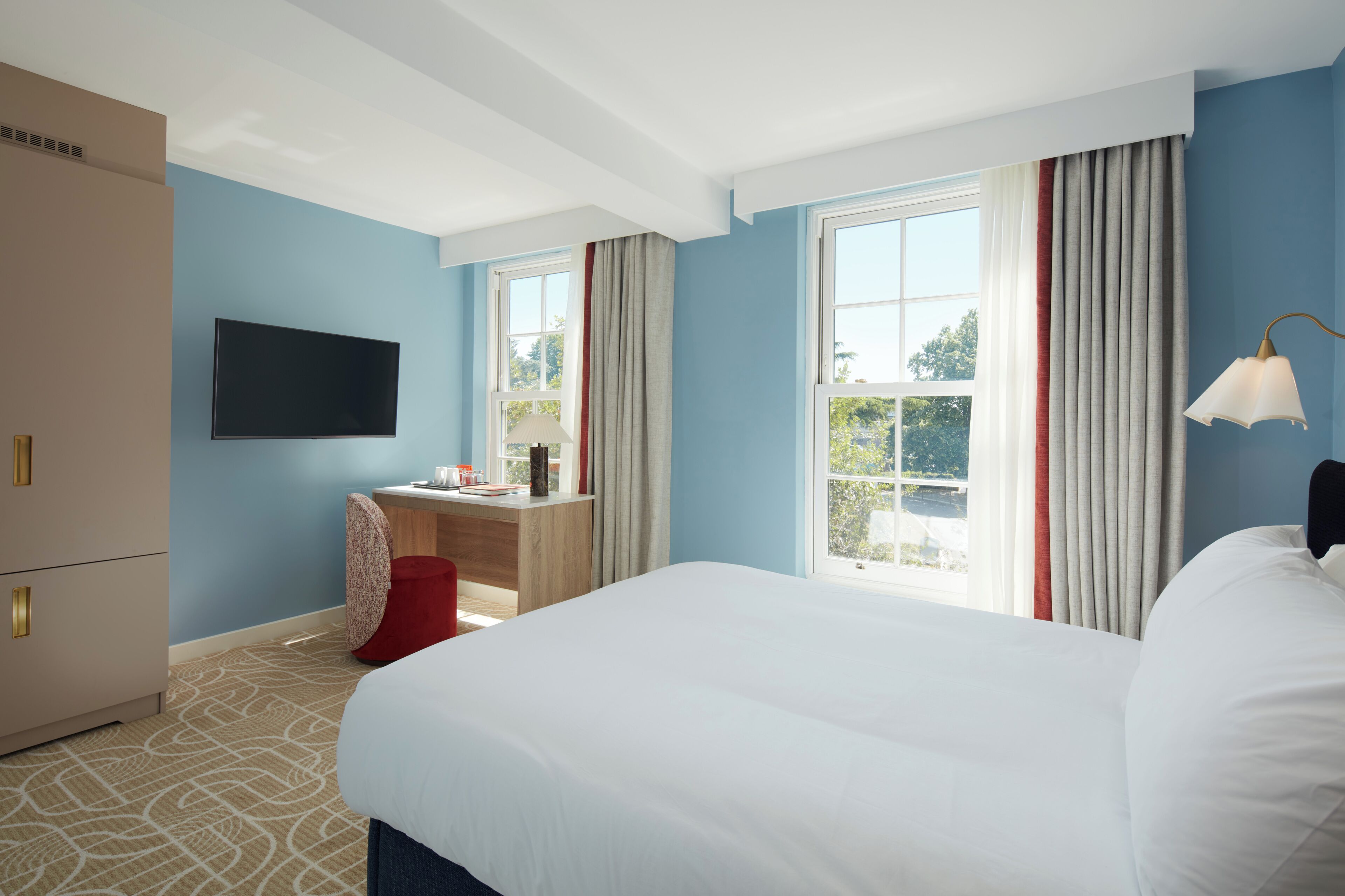 Ein Hotelzimmer mit Bett, Schreibtisch, Fernseher und einem Fenster mit Vorhängen.