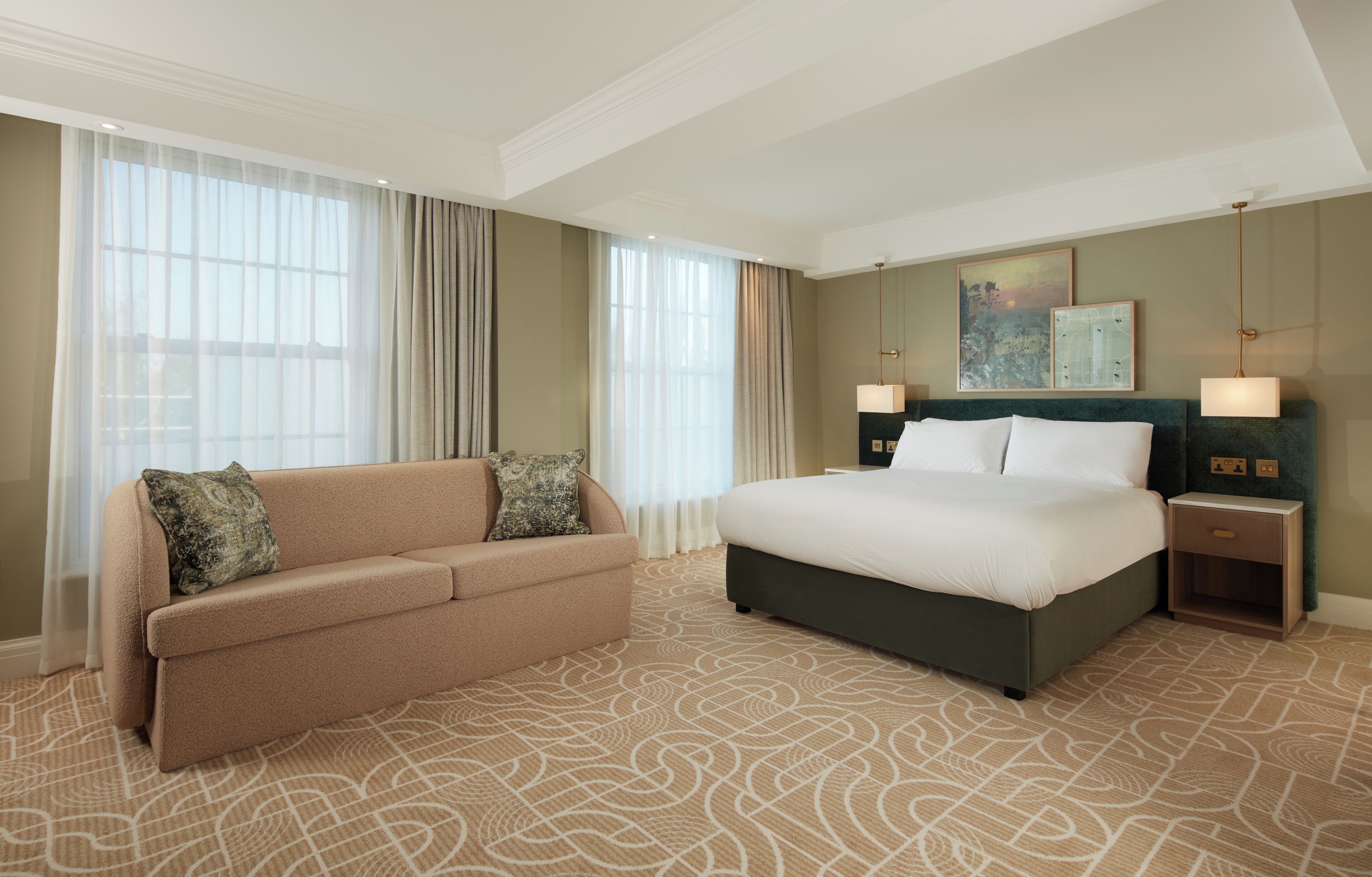 A hotel room with a bed, a sofa, a nightstand, and a large window with curtains.