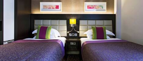 A hotel room with two beds, a headboard with a light fixture, and artwork on the wall.