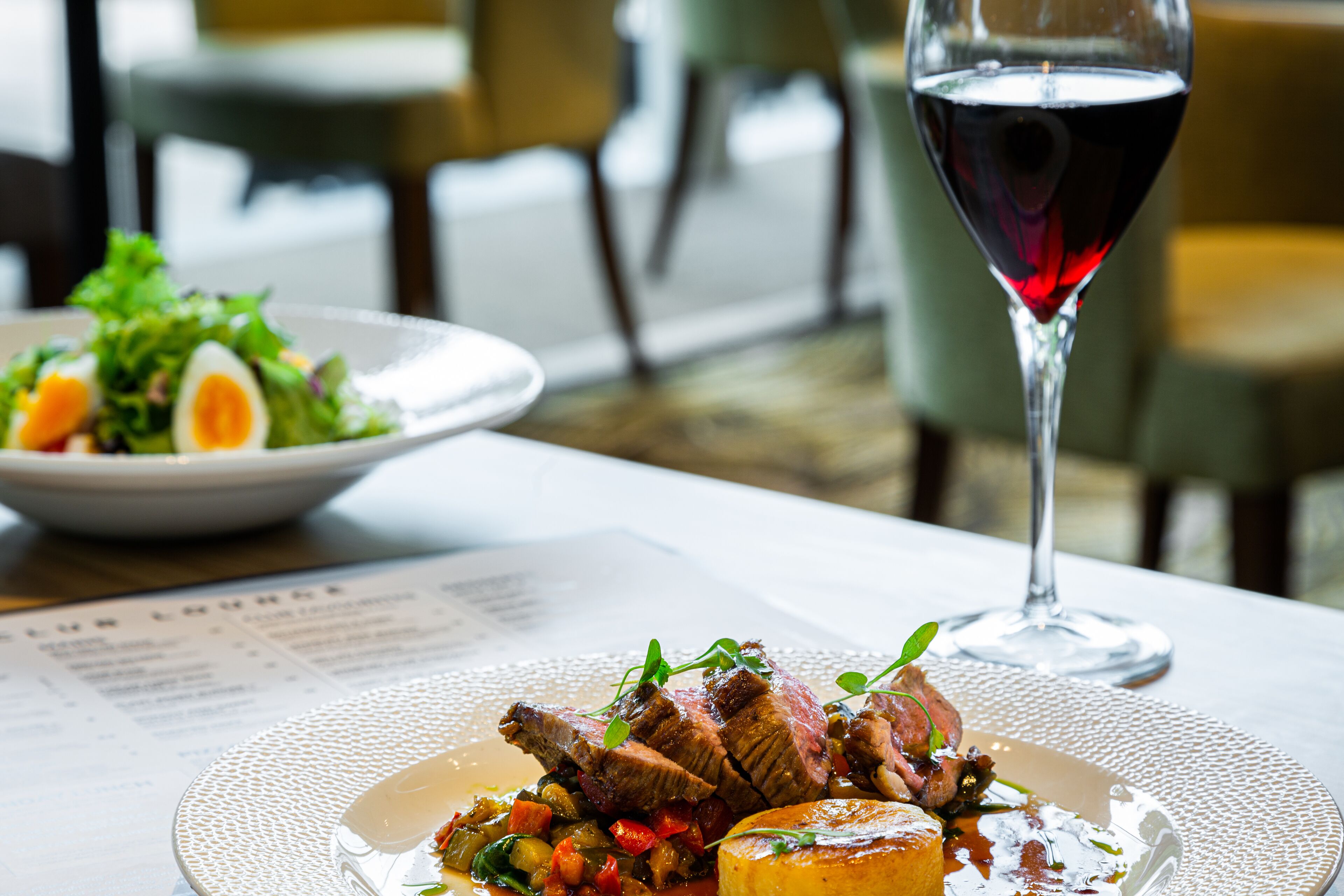A dining table with a plate of steak, vegetables, and a glass of red wine.