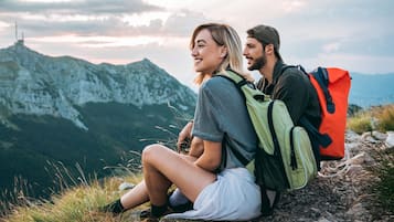 Dos personas sentadas sobre un afloramiento rocoso con mochilas, contemplando un paisaje montañoso.