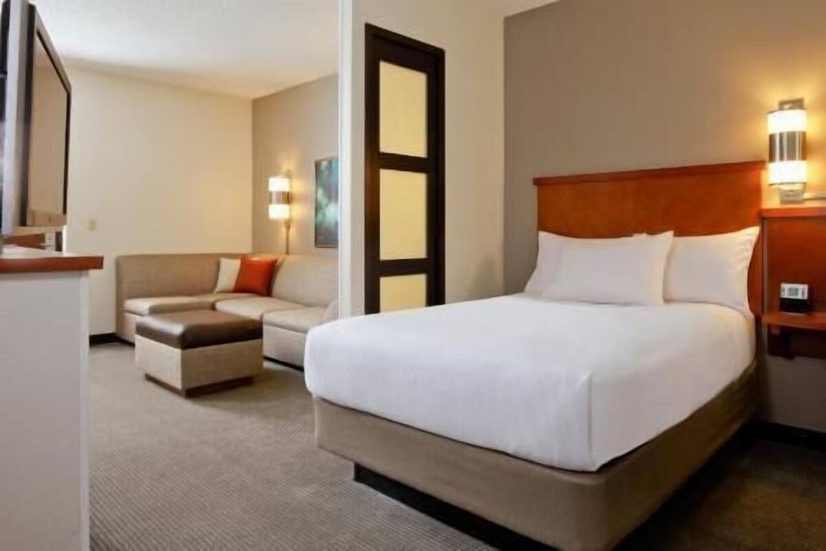 A hotel room with a bed, a sofa, a desk, and a door.