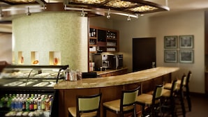 Zona de bar con mostrador curvo, taburetes, vitrina refrigerada con bebidas y una máquina de café.