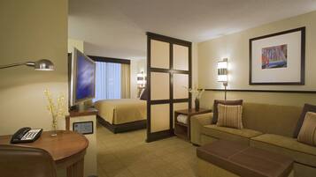 A hotel room with a bed, a sofa, a desk with a phone, a TV, and a painting on the wall.
