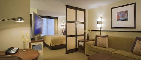 A hotel room with a bed, a sofa, a desk with a phone, a TV, and a painting on the wall.