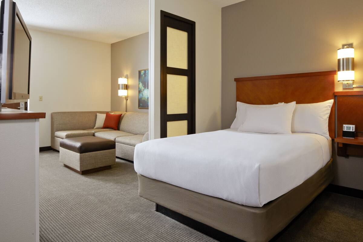 A hotel room with a large bed, a sofa, a small table, and a desk.