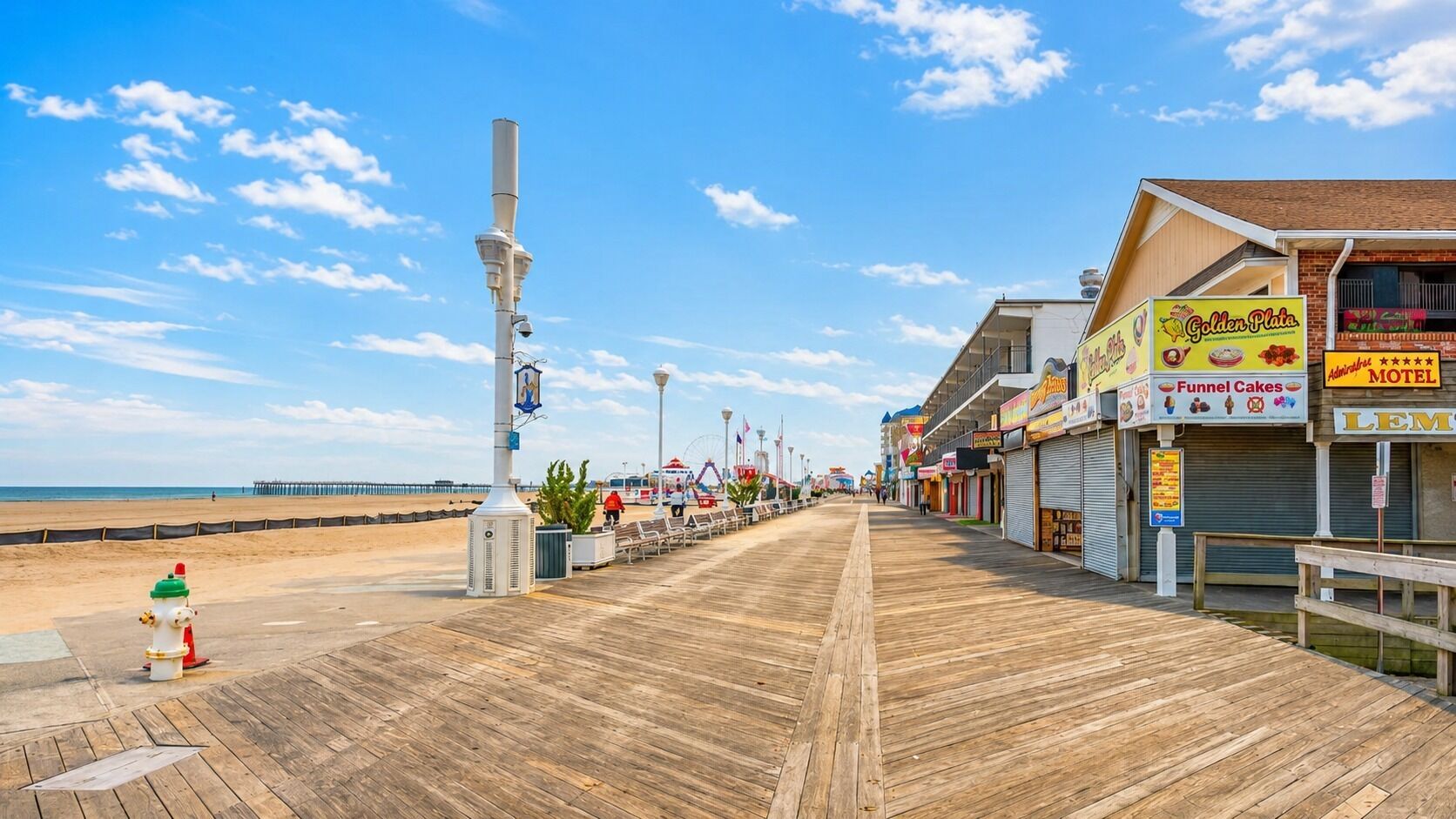 A boardwalk with shops and a beach in the background.