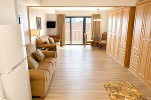 Amplia sala de estar con sofá, mesa de comedor con sillas, televisor montado en la pared y puerta corrediza de vidrio que da a un balcón exterior.