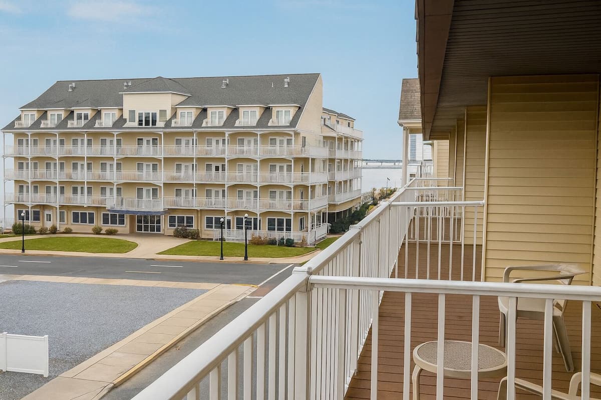 A multi-story hotel with balconies, a parking lot, and a view of the water.