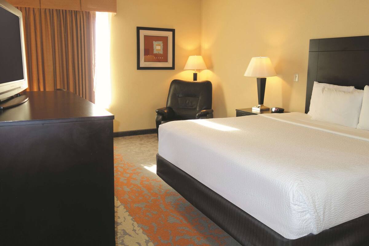 Habitación de hotel con una cama grande, un escritorio, una silla, dos lámparas de noche y un cuadro en la pared.