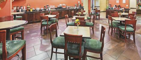 Un restaurant doté de nombreuses tables et chaises, d’un téléviseur fixé au mur, et d’une variété de distributeurs de nourriture et de boissons sur le comptoir.