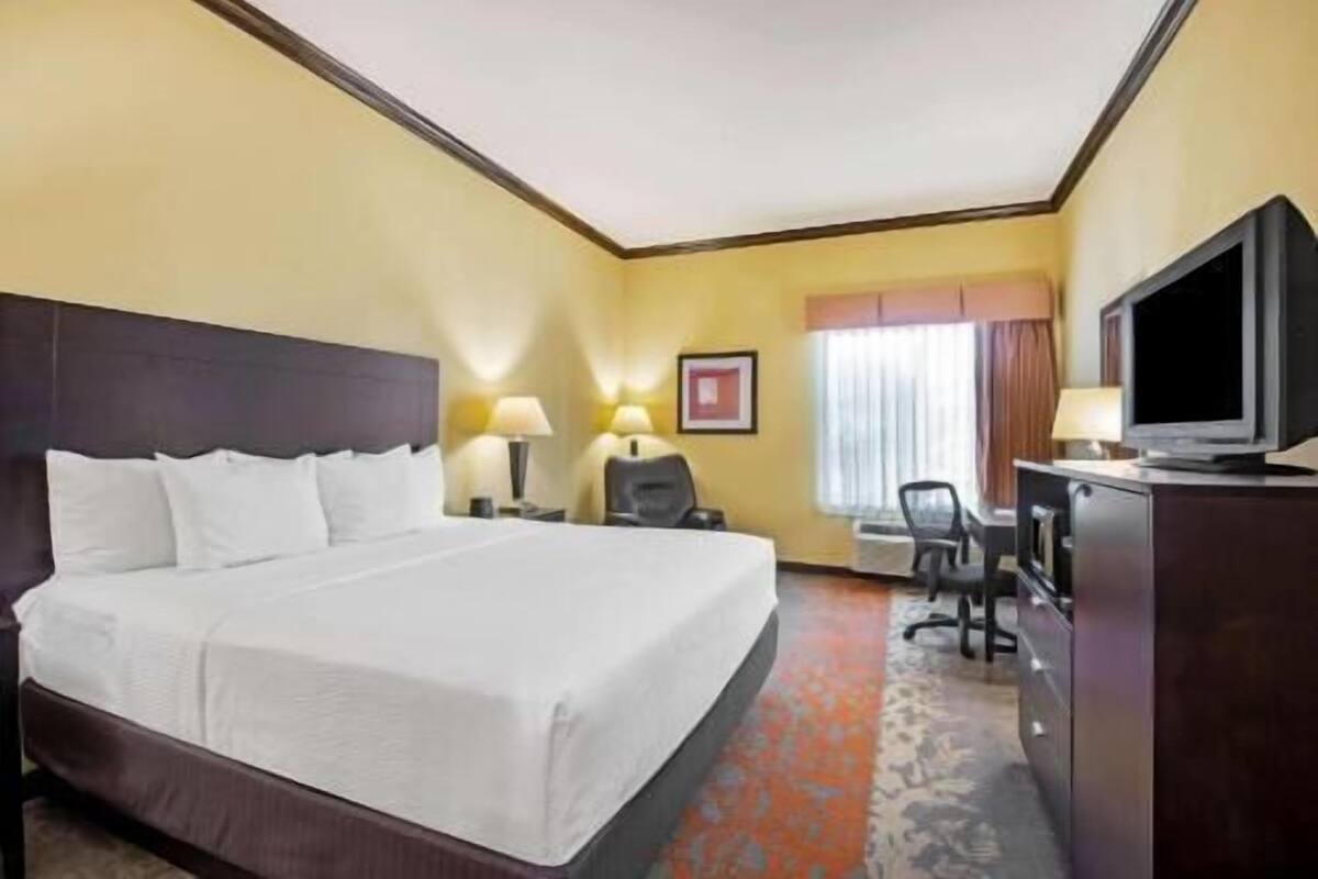 Habitación de hotel con una cama grande, un escritorio con silla, televisor y ventana con cortinas.