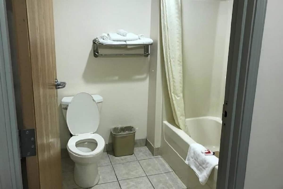 Un baño con inodoro, cubo de basura, repisa con toallas y bañera.