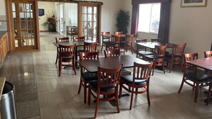 Een eetruimte met houten tafels en stoelen, een plafondventilator en een groot raam met gordijnen.