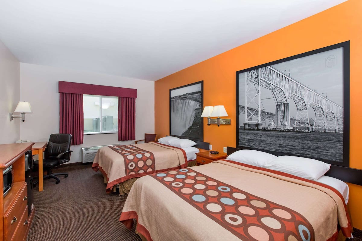 Habitación de hotel con dos camas, un escritorio, una silla y un ventanal con cortinas rojas.