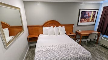 A hotel room with a large bed, a wooden headboard, a desk, a chair, a telephone, and a framed picture on the wall.