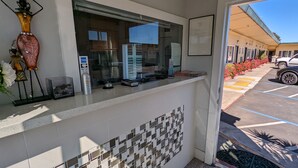 A reception area with a counter, decorative vases, and a view of a parking lot with a white vehicle. - Deluxe Inn (South San Francisco)