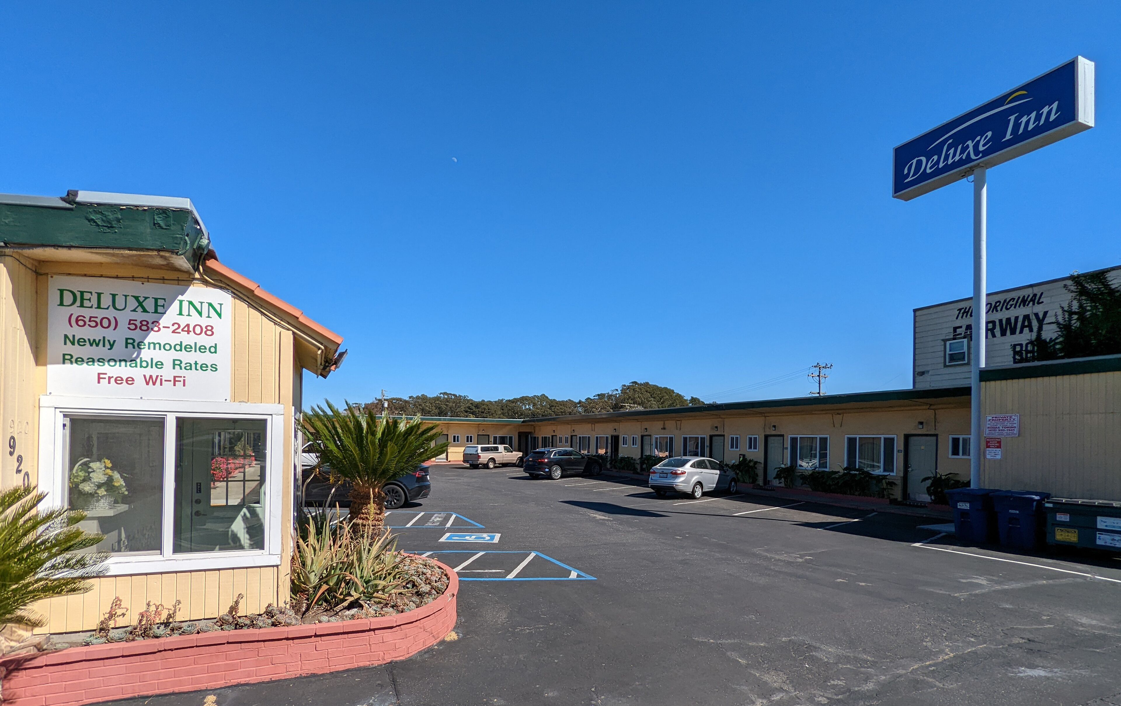 A hotel named DELUXE INN with a signboard, a parking lot, and a building in the background.