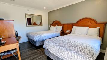 A hotel room with two beds, a wooden desk, a mirror, and a telephone.