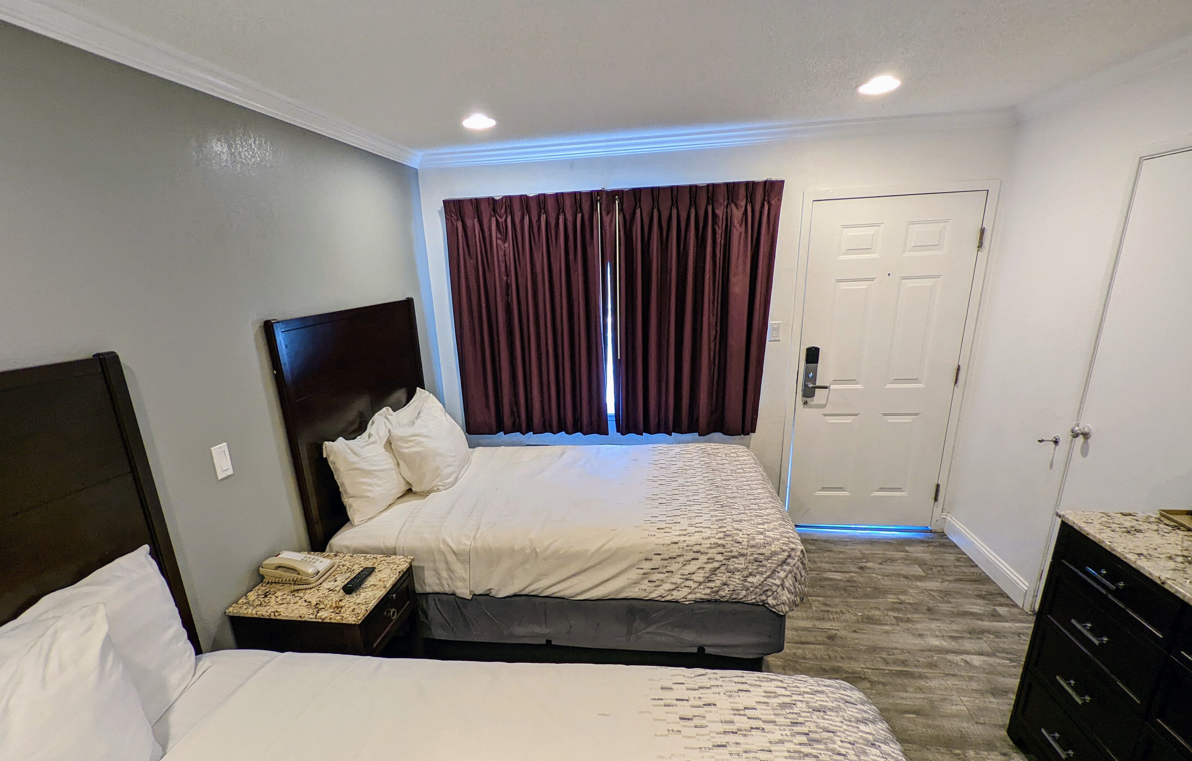 A hotel room with two beds, a desk with a telephone, a door, and a window with curtains.